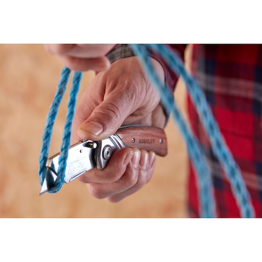 Stanley 0-10-073 folding knife cutting blue rope, close-up with wood handle and engraved logo.