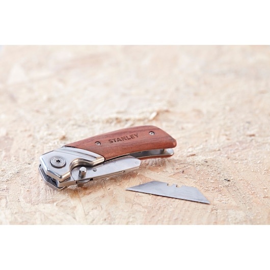 Photo of STANLEY 0-10-073 folding utility knife with wood handle and spare blade on wooden surface.