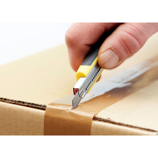 STANLEY 0-11-300 utility knife cutting brown tape on cardboard box, close-up photography.