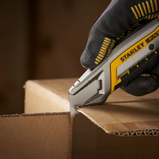 STANLEY 0-11-718 utility knife cutting cardboard, close-up photo showing gloved hand and blade.