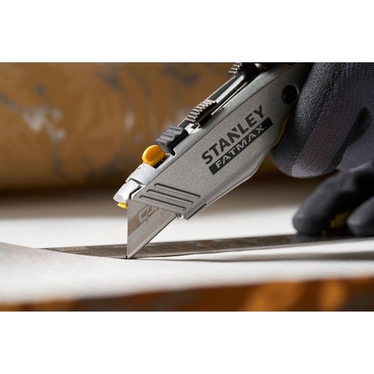 Photo of STANLEY 0-11-800 utility knife cutting material, close-up side angle, hand with glove visible.
