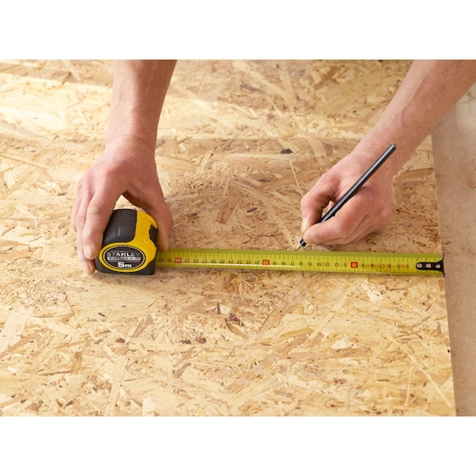 Photography of STANLEY 0-33-720 tape measure used to mark measurements on plywood surface.