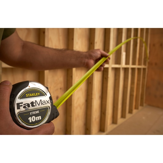 STANLEY 0-33-897 FatMax XTREME 10m tape measure held by hand in construction setting.