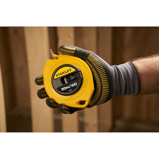 Stanley 0-34-107 yellow 20m tape measure held in gloved hand, photography construction setting.