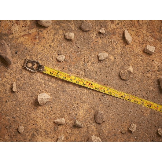 STANLEY 0-34-107 tape measure on dusty ground with scattered rocks, photography of product in use.