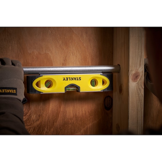 STANLEY 0-43-511 spirit level used on a horizontal pipe, close-up scene with gloved hand holding tool.