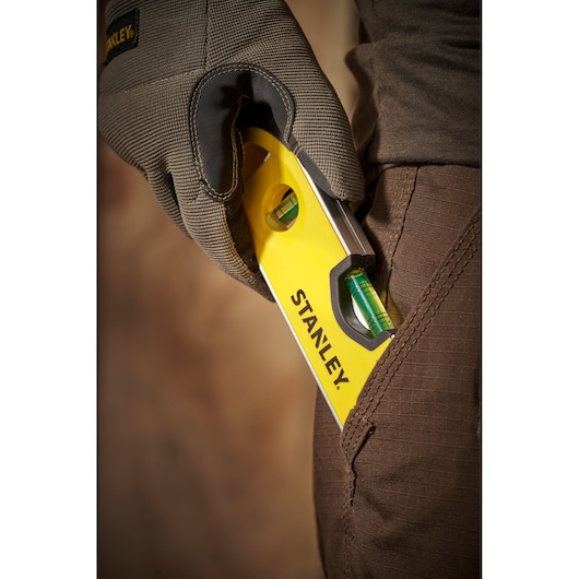 STANLEY 0-43-511 spirit level close-up, yellow body, held by gloved hand near brown pocket.