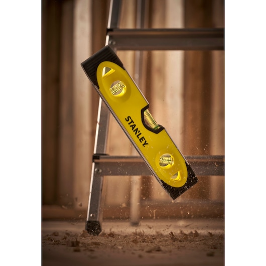 STANLEY 0-43-511 yellow spirit level with three vials leaning against a metal ladder, construction site background.