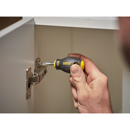 STANLEY 0-65-407 stubby screwdriver with black and yellow handle in use tightening a cabinet hinge.