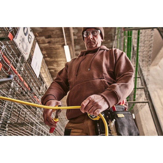 STANLEY 0-84-004 photography of worker using pliers to cut yellow cable, tool pouch visible, industrial setting.