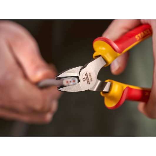 STANLEY 0-84-009 insulated diagonal cutting pliers with red and yellow handles cutting a wire, close-up.
