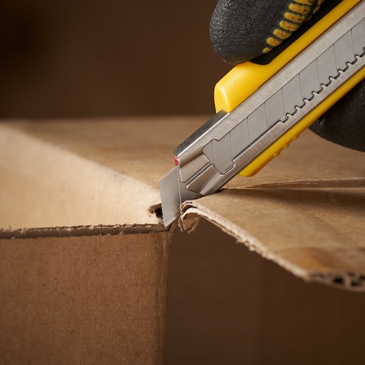 STANLEY 1-11-300 utility knife cutting cardboard, close-up side view.