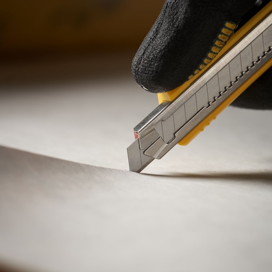 STANLEY 1-11-300 utility knife cutting paper, close-up side view, yellow and silver body, photography.
