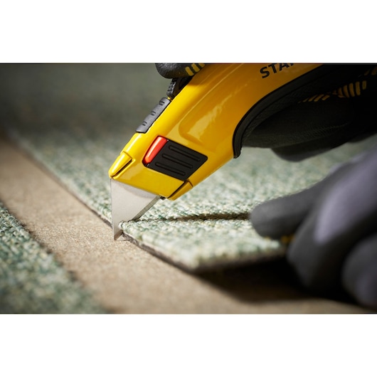 STANLEY 1-11-700 utility knife cutting carpet, close-up photography highlighting yellow handle and blade.