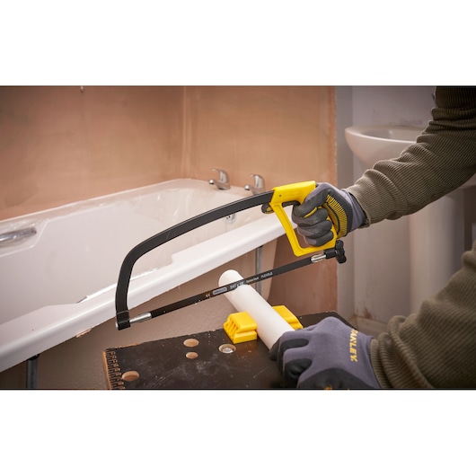 STANLEY 1-15-122 hacksaw cutting white PVC pipe in bathroom, close-up action shot.