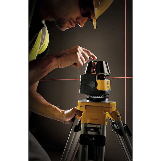 STANLEY 1-77-322 laser level on tripod projecting red lines, used by worker in construction setting.