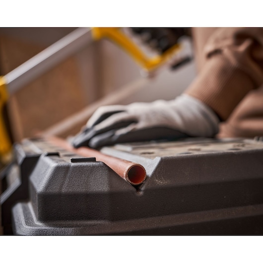 STANLEY 1-79-206 photography of gloved hand holding copper pipe on black workbench, close-up view.