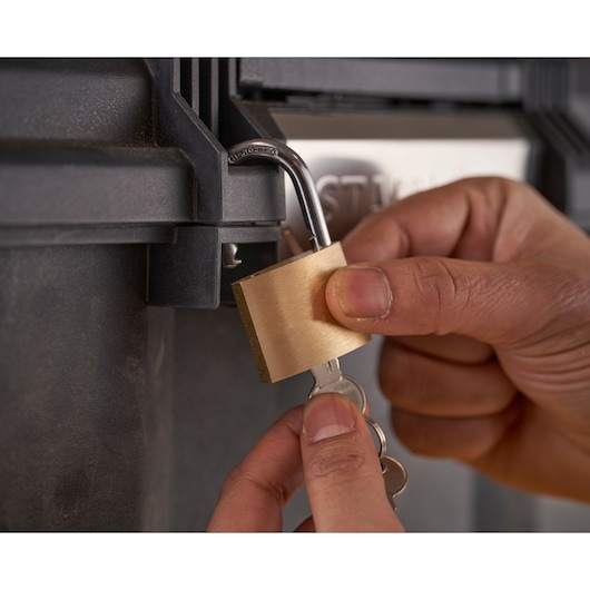 STANLEY 1-79-206 brass padlock being unlocked by hand on black storage box, close-up photography.