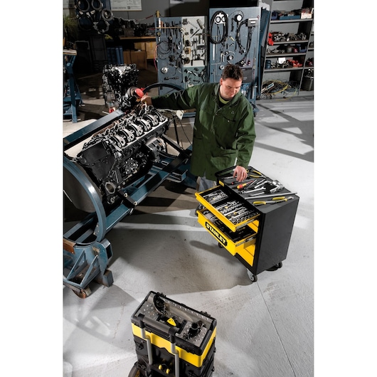 STANLEY 1-94-737 tool trolley with drawers open, yellow and black, in a workshop near engine repairs.