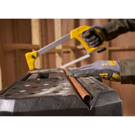 STANLEY 1-97-510 photography showing gloved hands cutting copper pipe with yellow hacksaw on black workbench.
