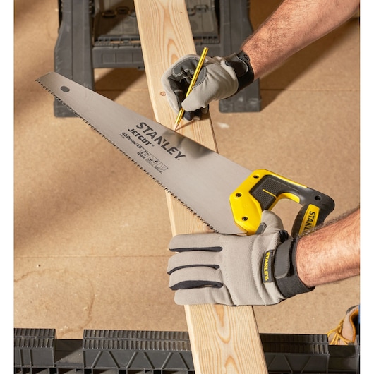 STANLEY 2-15-283 hand saw with yellow handle held by gloved hand marking wood plank, angled view.