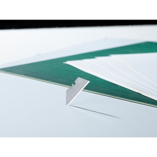 STANLEY 3-11-908 utility blade standing upright on table, green cutting mat and white sheets in background, side angle.