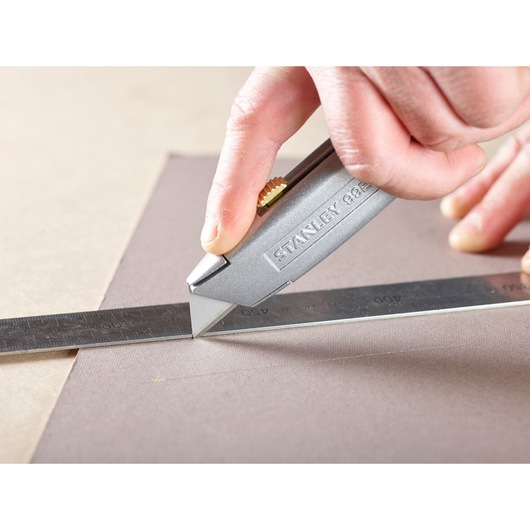 Stanley 3-11-908 utility knife cutting along a metal ruler on a flat surface, close-up photography.