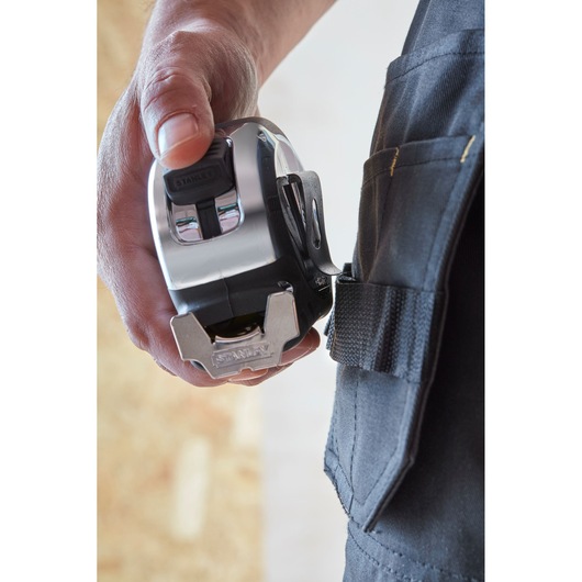 Photo of STANLEY 33-894 tape measure with metal clip, held by hand near tool belt pocket.