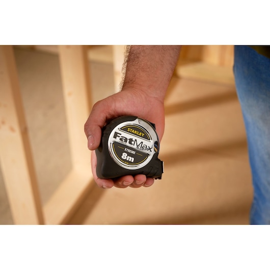 STANLEY 33-894 tape measure FatMax 8m, black and silver, held in hand, indoor construction site.