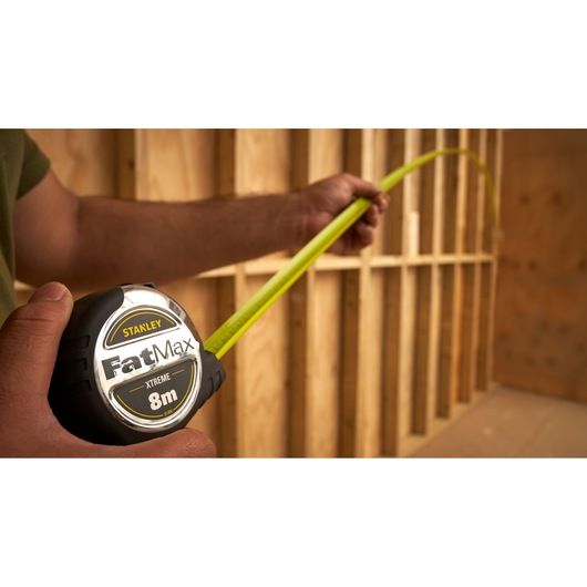 STANLEY 33-894 tape measure FatMax 8m, in use, close-up, with yellow blade extended in construction setting.