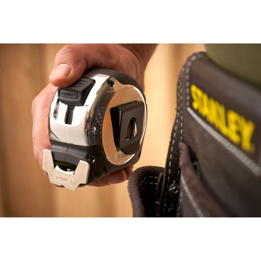 Photo of STANLEY 5-33-891 tape measure in hand next to tool belt with STANLEY logo, close-up view.