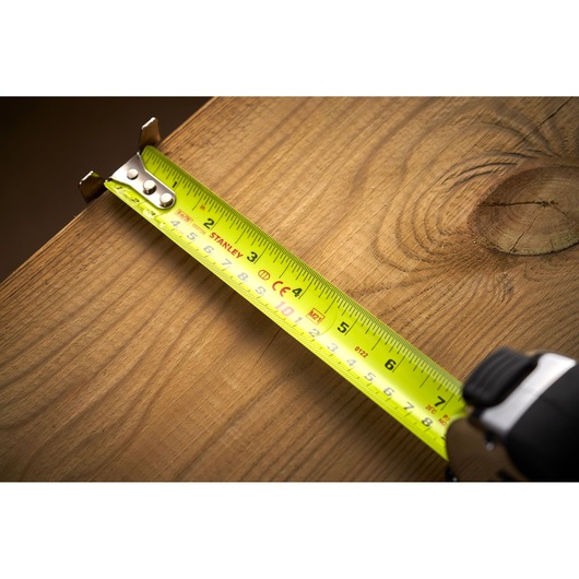 Photo of STANLEY 5-33-891 tape measure extended across wooden surface, yellow tape with black markings visible.