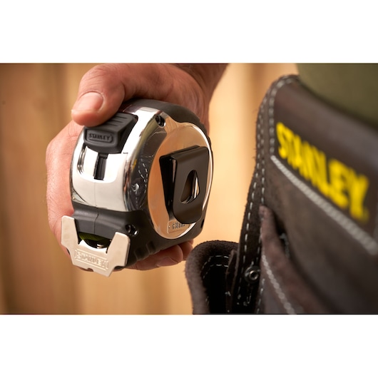STANLEY 5-33-894 tape measure held in hand near tool belt, close-up showing chrome finish and clip.