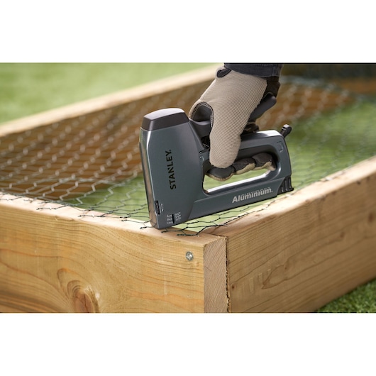 STANLEY 6-TR250 aluminum staple gun, close-up, used to attach wire mesh to wooden frame.