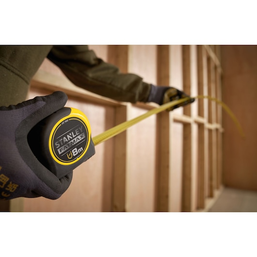 Stanley FMHT0-33868 tape measure with yellow blade extended in a construction framing setting.