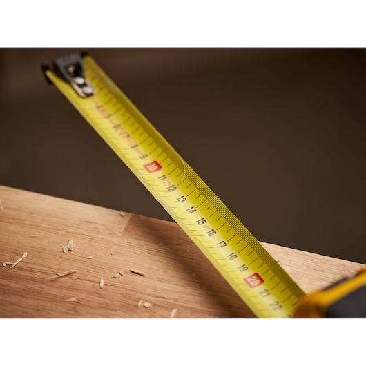STANLEY FMHT0-33868 tape measure in use, yellow blade extended over wooden surface with wood shavings, close-up.
