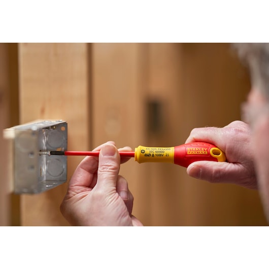 Stanley FMHT0-62649 insulated screwdriver used to tighten screw in metal electrical box, close-up view.