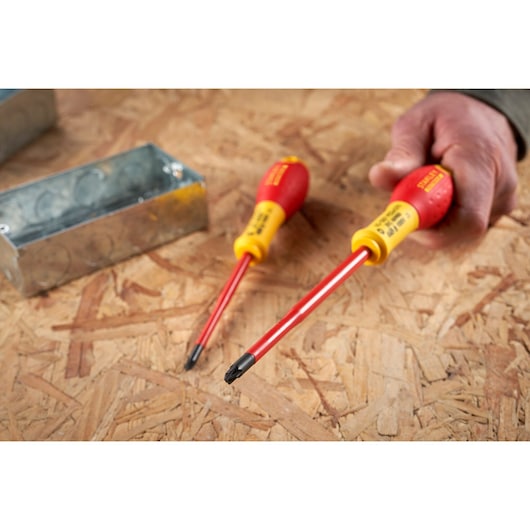 STANLEY FMHT0-62649 insulated screwdriver with red and yellow handle, shown in use on plywood surface.