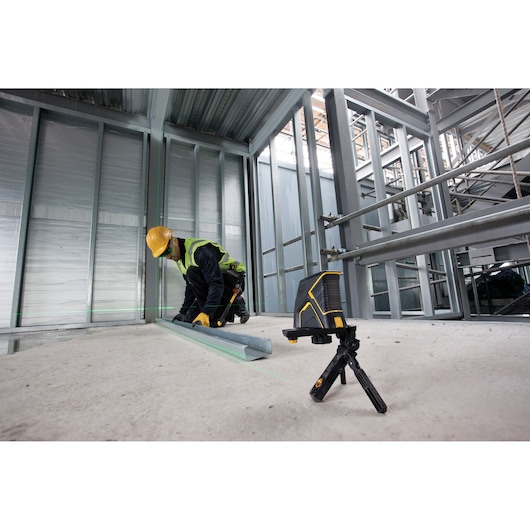 STANLEY FMHT1-77348 laser level on tripod at construction site, worker aligns metal beam using green laser lines.