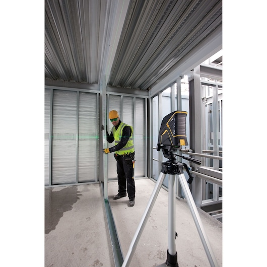STANLEY FMHT1-77348 laser level on tripod used at construction site, worker aligns metal framing.
