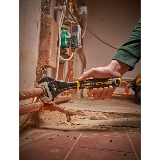 Photo of STANLEY FMHT13125-0 adjustable wrench being used on copper pipes in a plumbing setting.