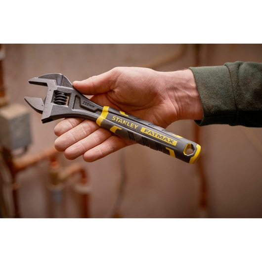 Stanley FMHT13128-0 adjustable wrench with yellow and black handle held in hand, indoor setting.