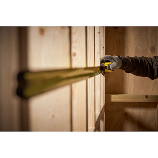 STANLEY FMHT33103 tape measure extended along wooden wall in workshop, side angle view.