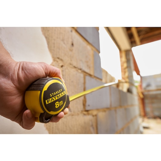 Photo of STANLEY FMHT33103 tape measure, yellow and black, used to measure a brick wall during construction.