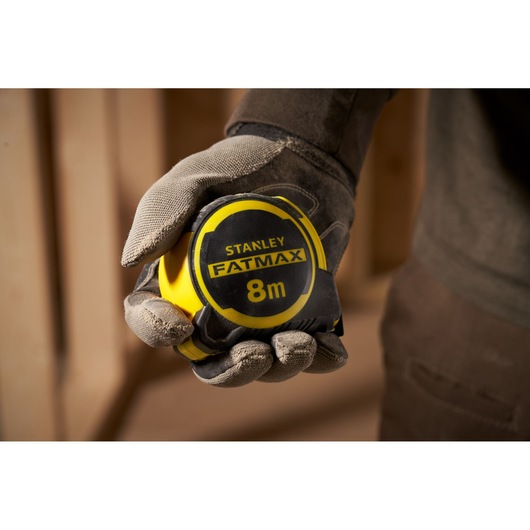 Photo of STANLEY FATMAX FMHT33103 tape measure, 8m, yellow and black, held in a gloved hand.