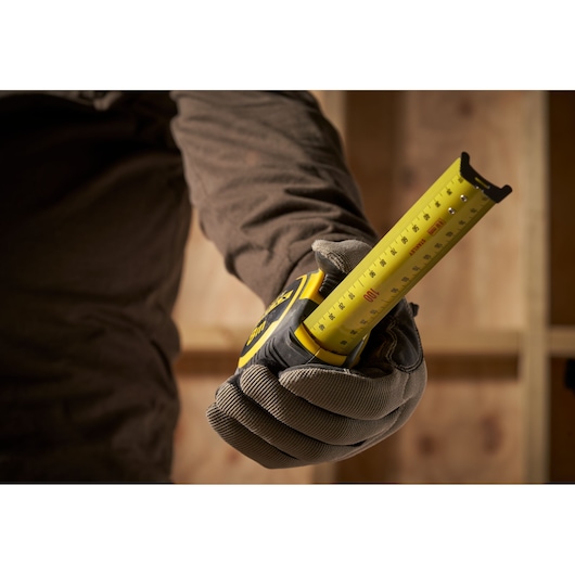 Stanley FMHT33103 tape measure held by a gloved hand, yellow blade extended, construction background.