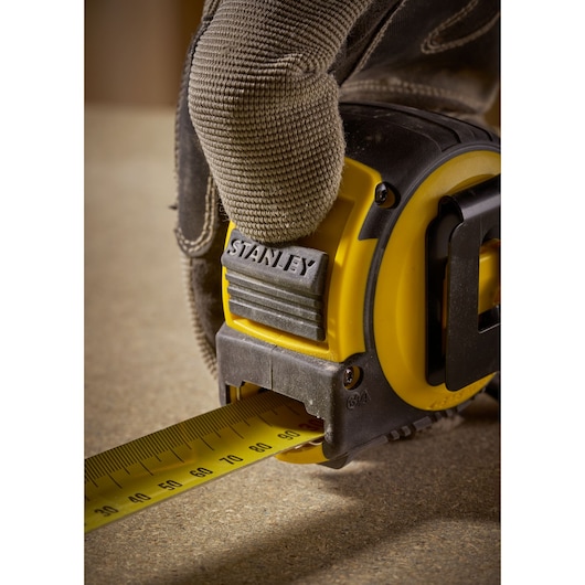 STANLEY FMHT33103 tape measure in use, yellow and black, close-up of gloved hand pulling tape.