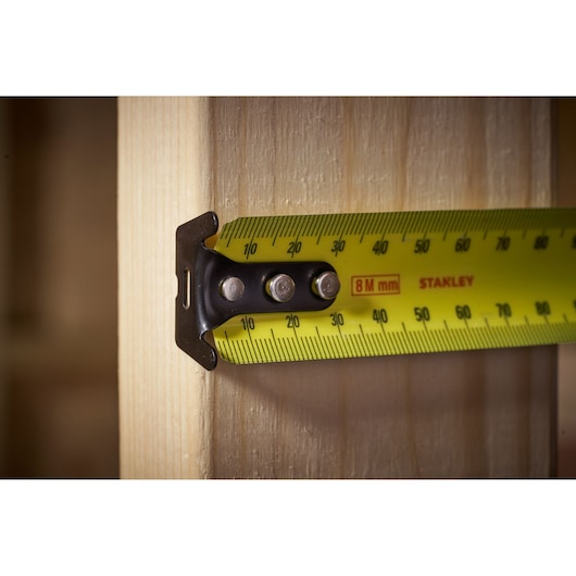 Photo of STANLEY FMHT33103 tape measure with yellow blade measuring wood, close-up side view.