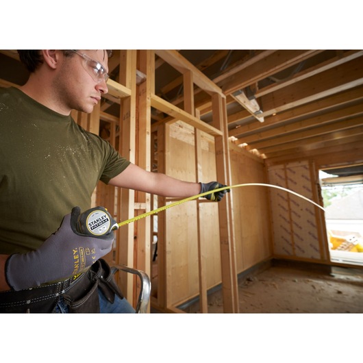 Photo of STANLEY FMHT38215-5 tape measure extended by worker wearing gloves, measuring in a building under construction.
