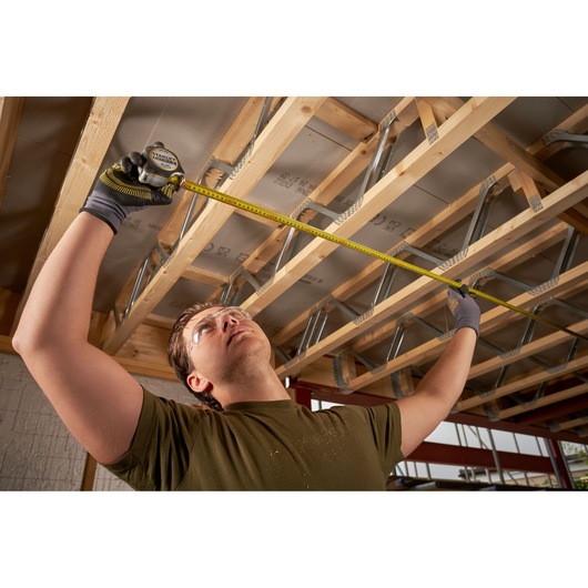 Photo of STANLEY FMHT38215-5 tape measure used by a person measuring wooden beams indoors.